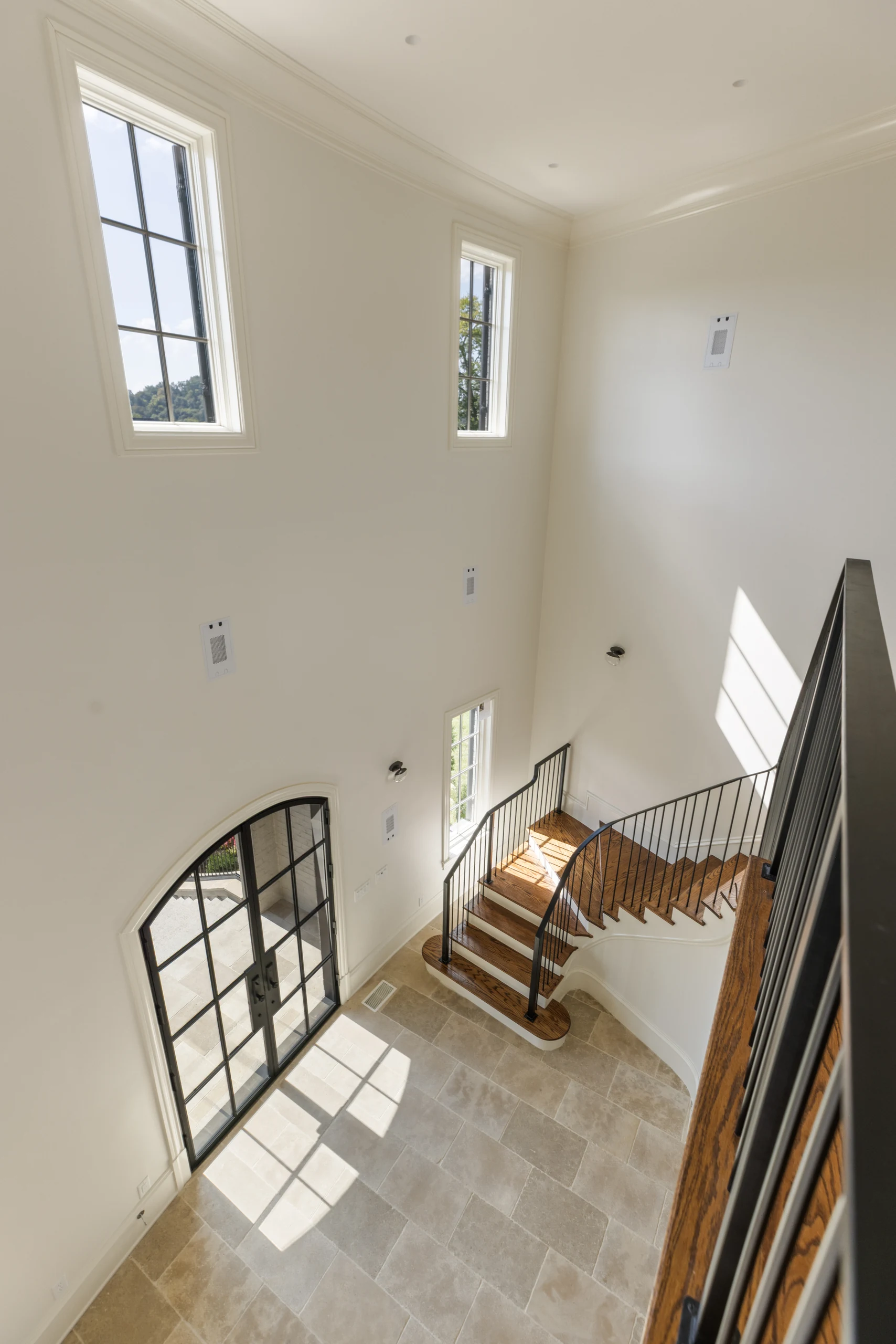 View down an iron-railed wooden staircase toward the sunlit limestone entry