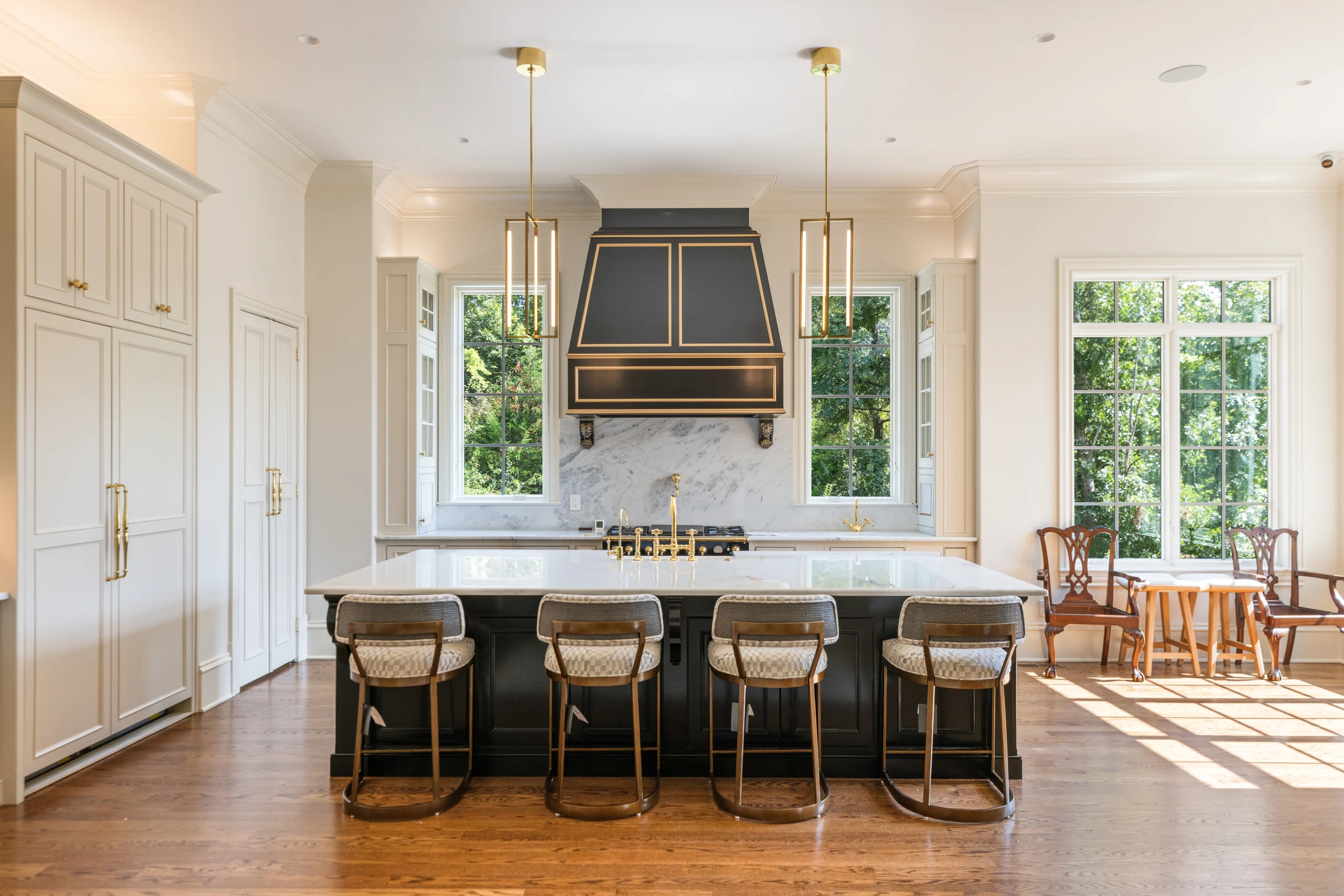 Cream kitchen cabinetry surrounding a dark island and brass-trimmed range hood
