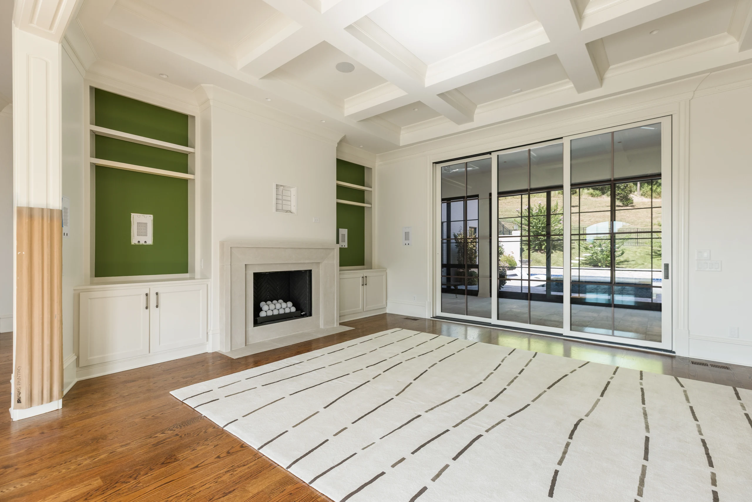 Living room with a coffered ceiling, green-backed shelving, and stone fireplace