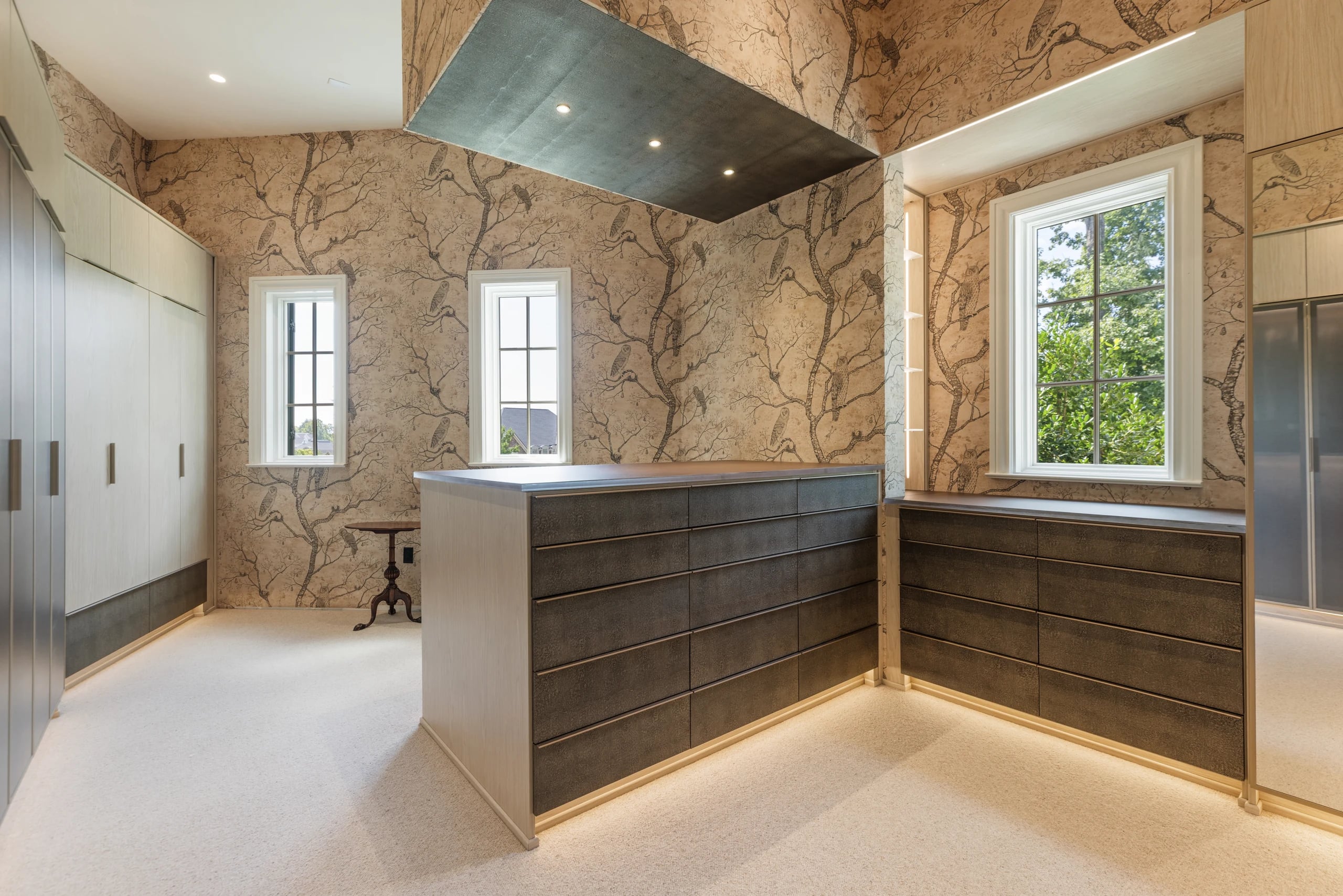 Master closet with wood cabinetry, an island, and patterned walls and ceiling