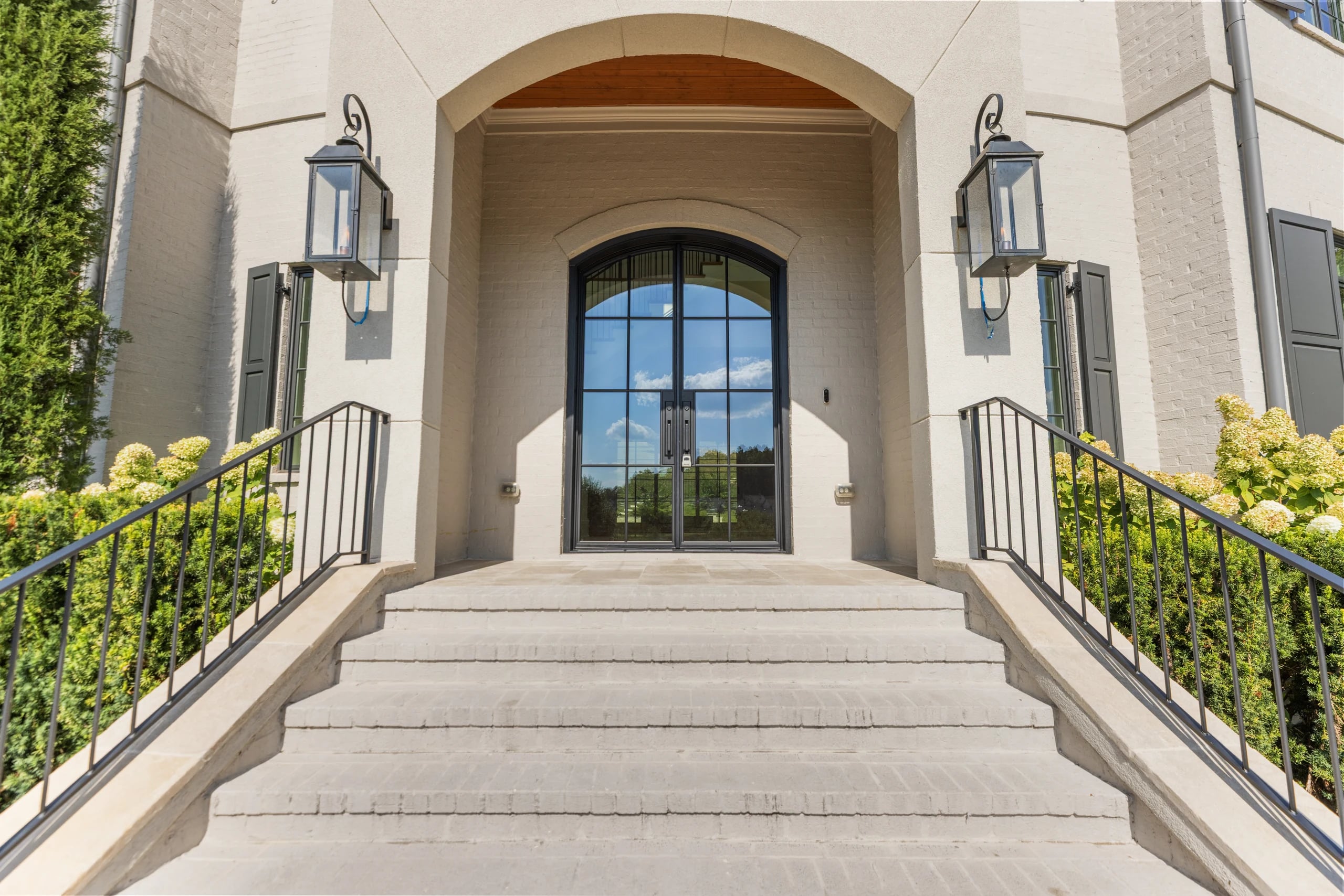 Stone entry steps leading to an arched glass door between two wall lanterns