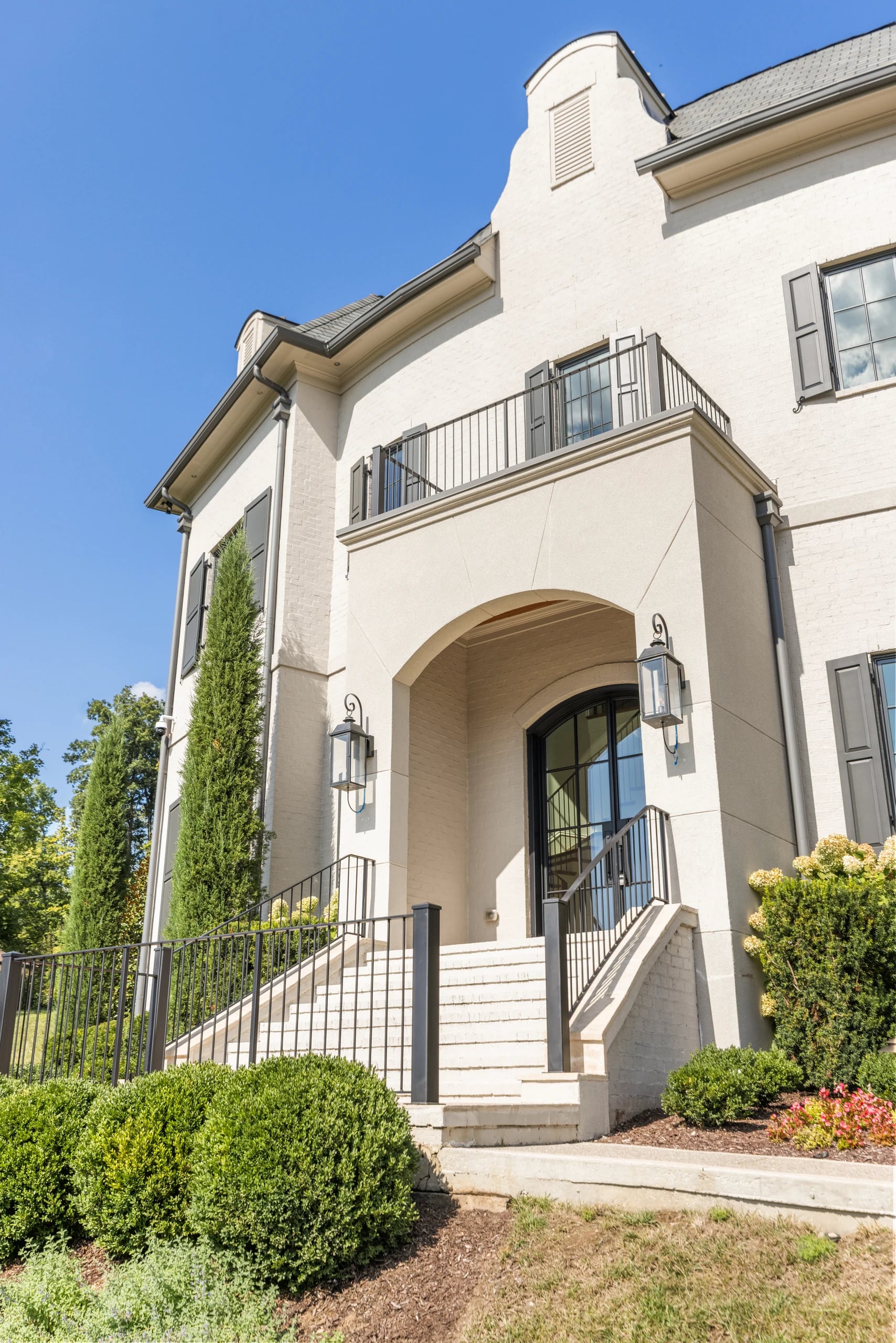 Tall stucco facade with an arched entrance, stone steps, and iron railings