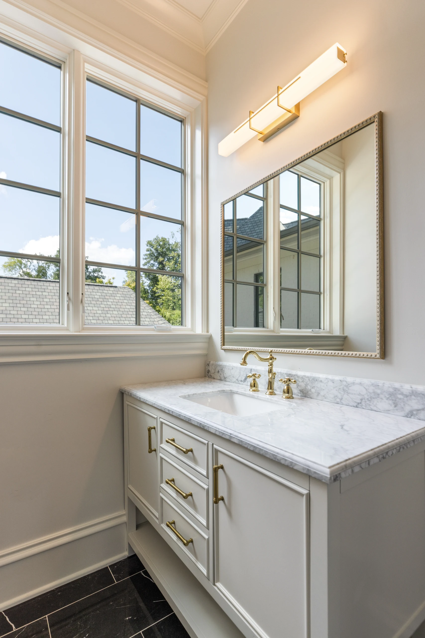 Powder room vanity with a stone counter and mirror beside a tall window