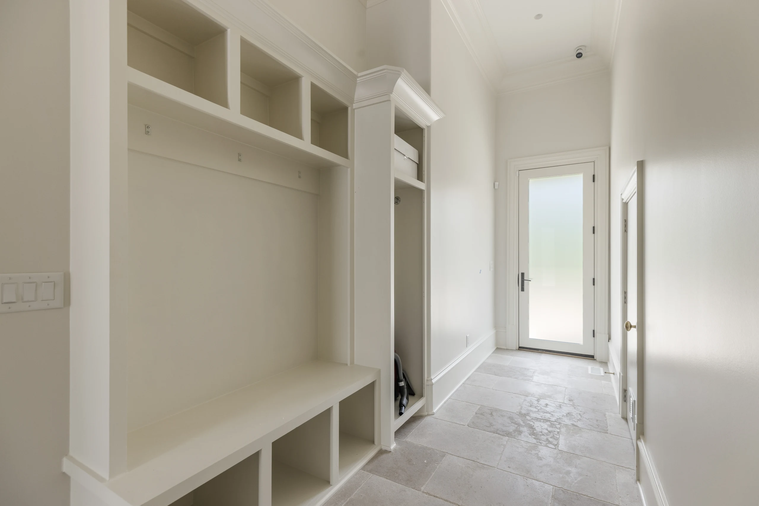 White mudroom storage with a built-in bench, open cubbies, and limestone floor